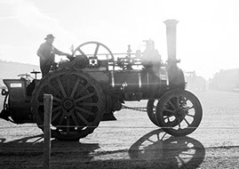 A  working steam engine pulling up a hill as the sun goes down.